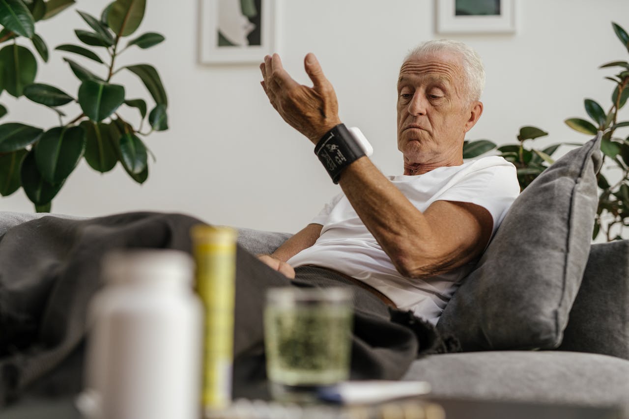 DHS Home-Care Services Elderly man checks his blood pressure using a wrist monitor in a comfortable living room setting.